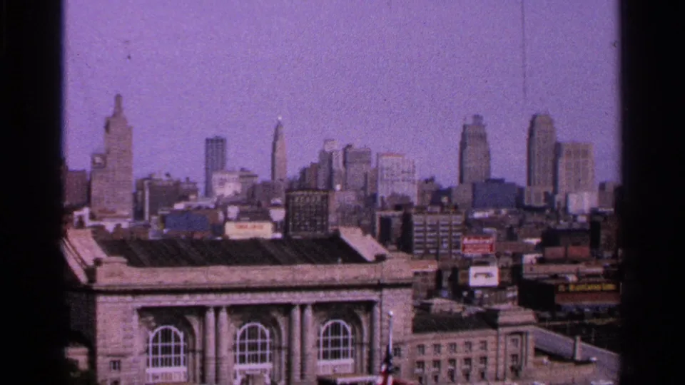 Kansas City skyline from the 1965 home movie, with downtown high-rises, rooflines, visible signs, and a large arched-window facade in the foreground.