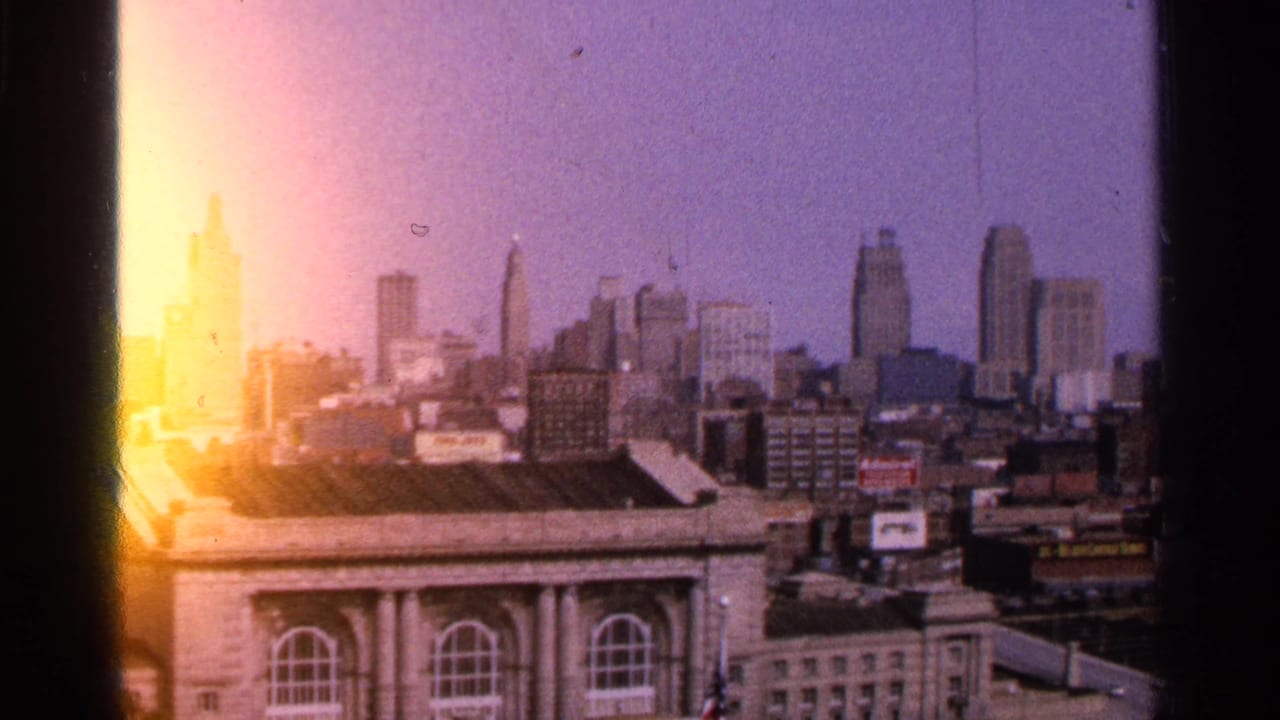 1965 Kansas City, Missouri skyline seen from an elevated position, with a large classical-style building in the foreground and bright 8mm film flare along the frame edge.