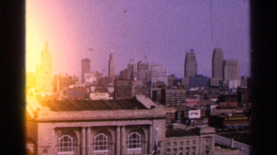1965 Kansas City, Missouri skyline seen from an elevated position, with a large classical-style building in the foreground and bright 8mm film flare along the frame edge.