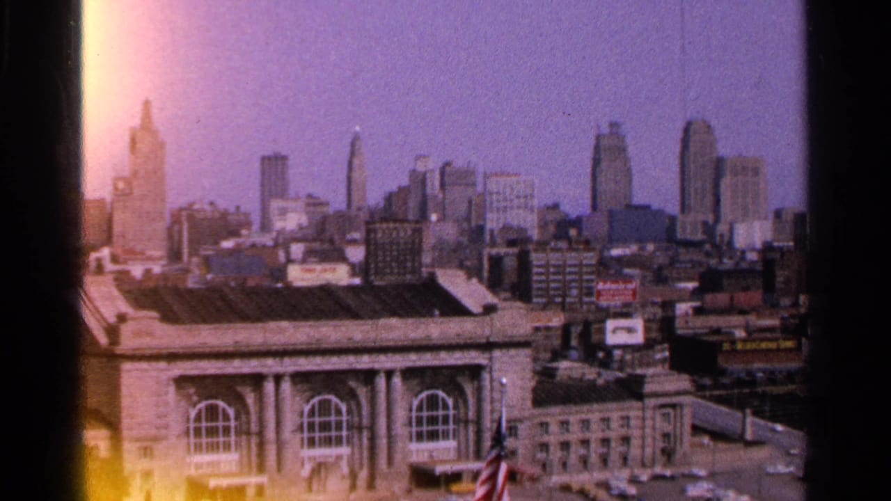 City skyline and large classical-style building with rooftop signs and a small American flag.