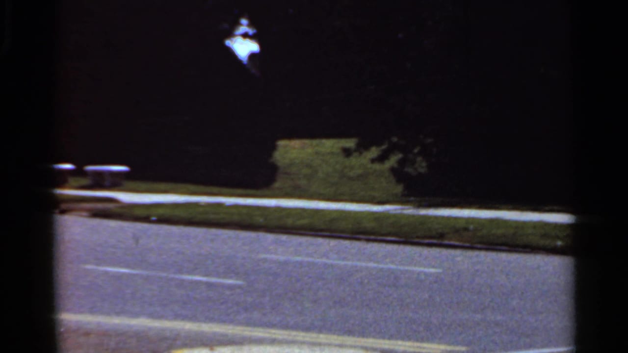 Dark street with white lane markings, grass, trees, and heavy shadow.