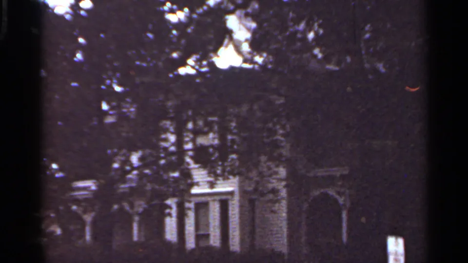 The final frame holds on a tree-obscured house exterior in the supplied 1965 Kansas City nighttime street footage.