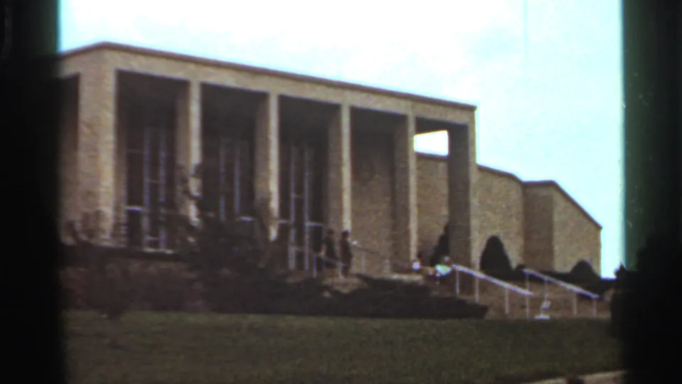 1965 Kansas City frame showing a modernist columned building with a broad stairway, lawn, and several people walking near the entrance.