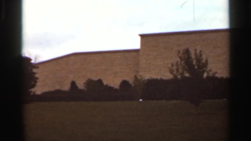 1965 Kansas City 8mm frame with an open grass foreground, dark landscaping, and a plain flat-roofed building in the background.