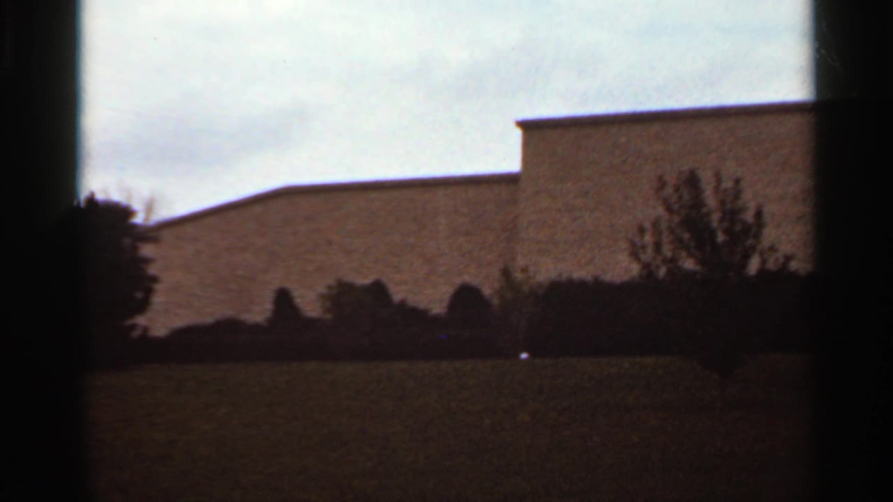 Low building exterior with lawn and shrubs seen through dark film-frame edges.