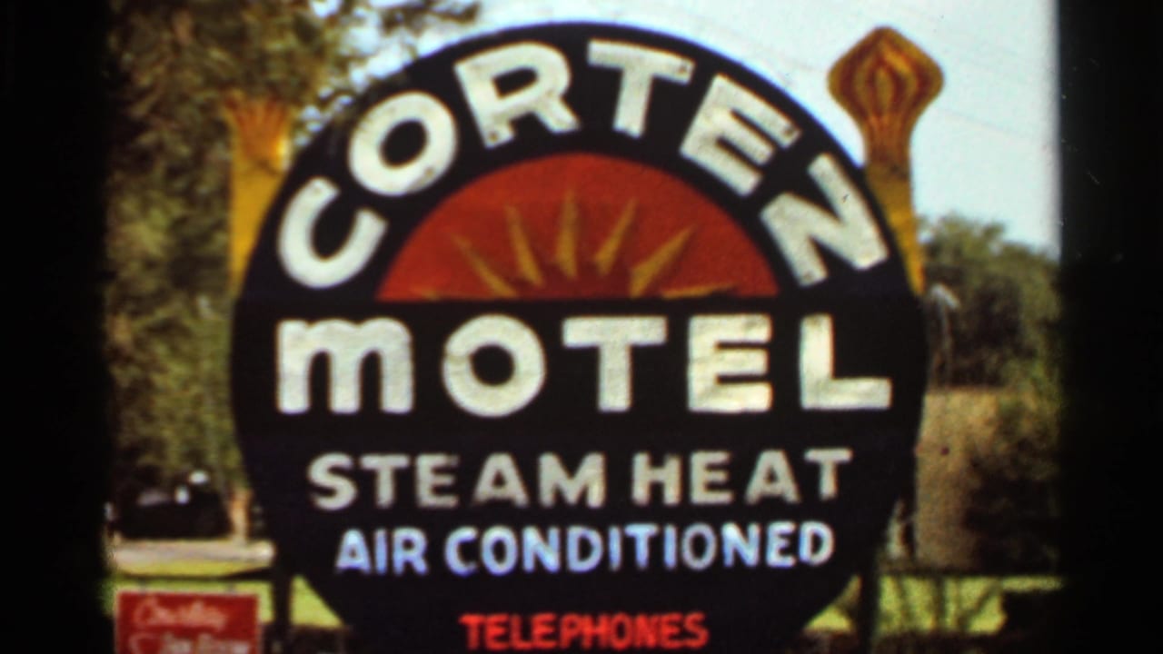 Cortez Motel sign advertising steam heat, air conditioning, and telephones beside trees.