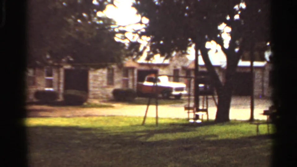 1965 Kansas City residential yard with a swing set in front of a stone house and a red-and-white pickup in the driveway.