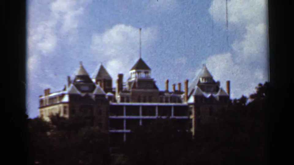 Faded 8mm frame showing the same turreted landmark building in Eureka Springs area, partly obscured by trees.