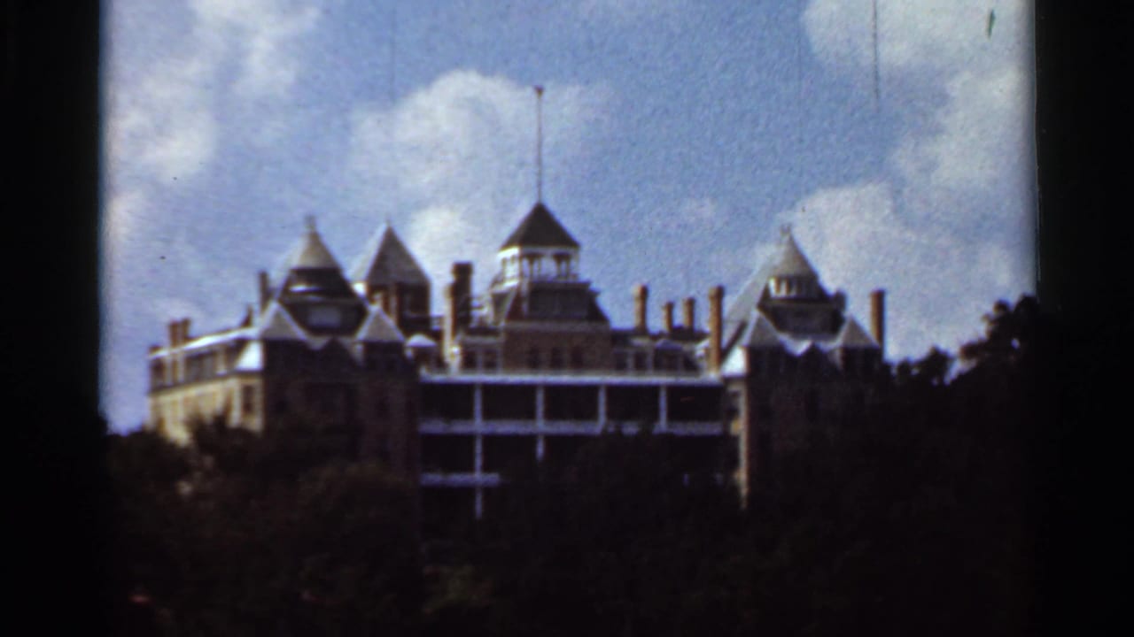 1965 Kansas City home-movie frame showing a turreted building above dark trees beneath a bright blue sky.