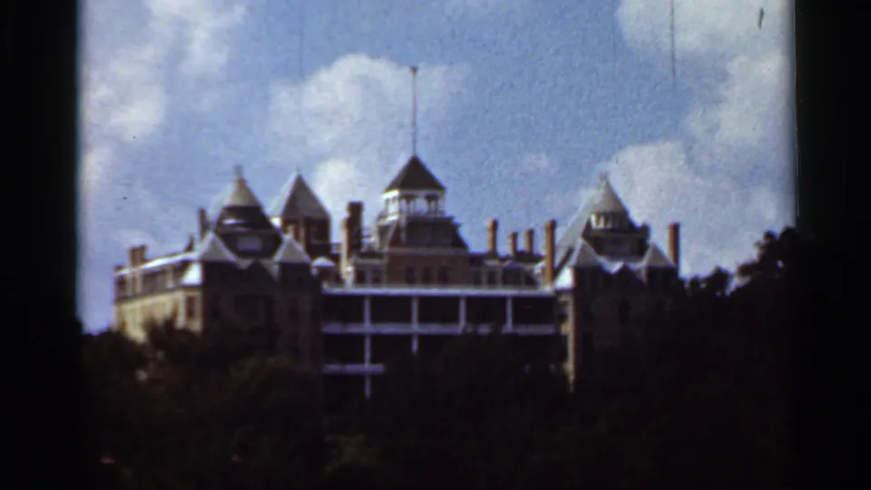 1965 Kansas City home-movie frame showing a turreted building above dark trees beneath a bright blue sky.