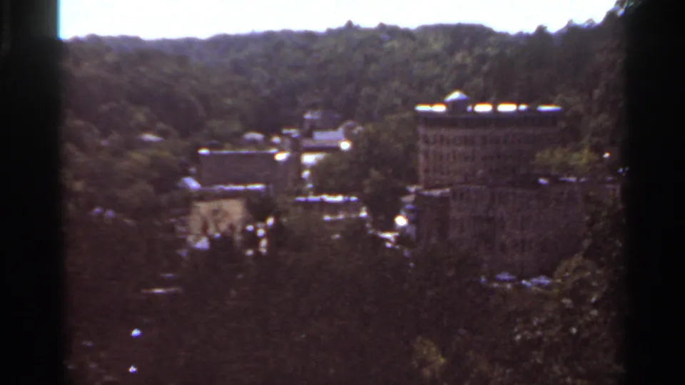 Soft 8mm view of buildings set among trees on a wooded Kansas City hillside, based on clip metadata.