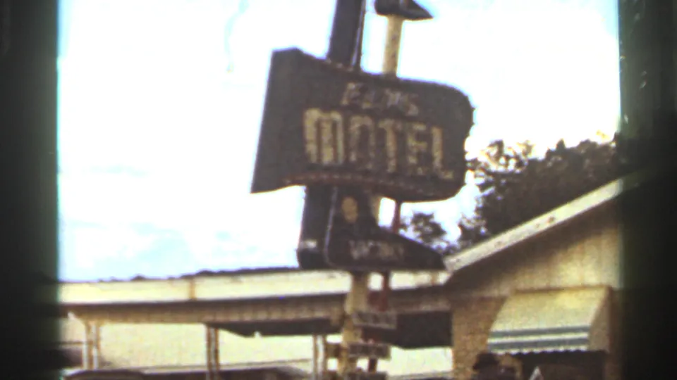 Close 1965 Kansas City home-movie view of a roadside motel sign against bright sky and a nearby roofline.