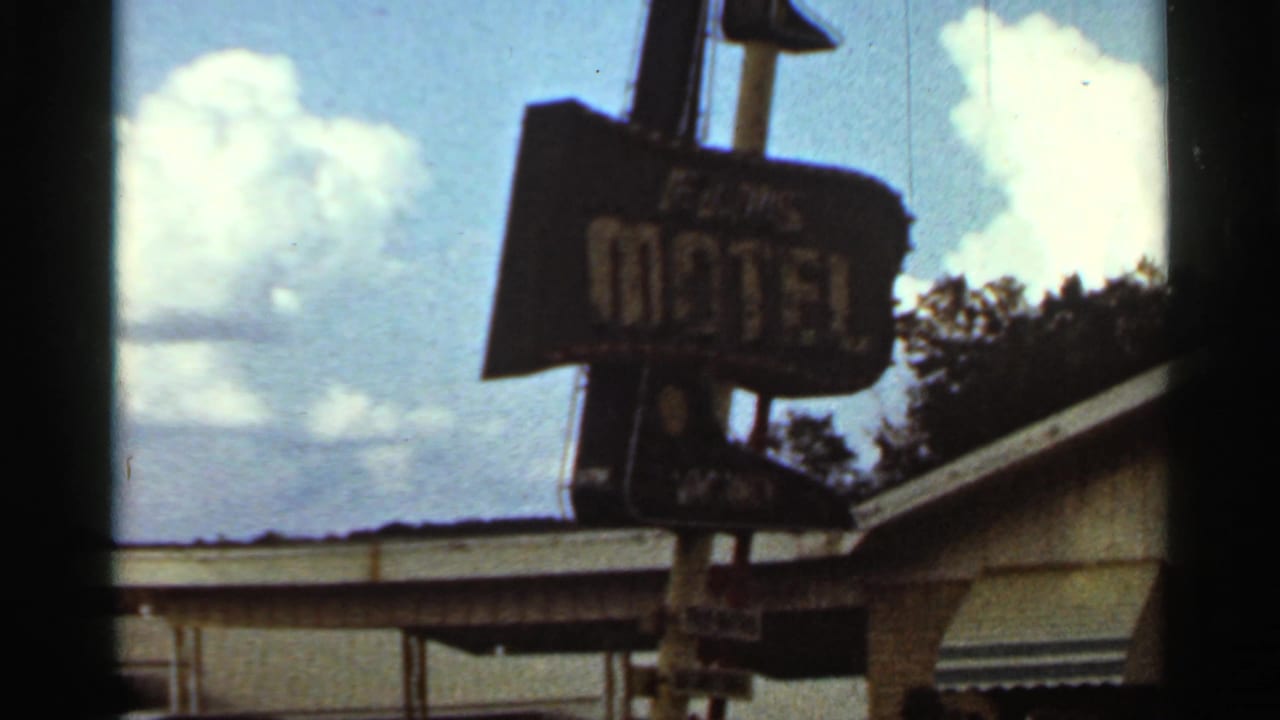 Weathered Elms Motel sign seen above a low roofline under blue sky and clouds.