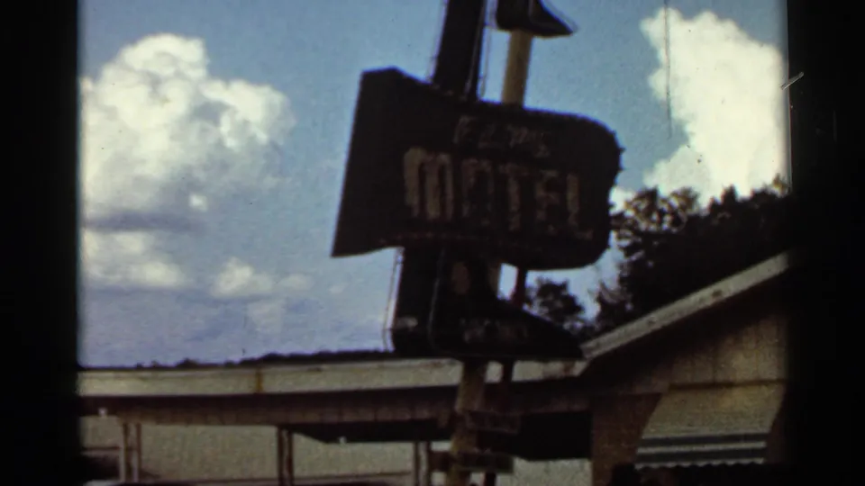 A soft 8mm view of the Elms Motel sign in Kansas City, with white lettering, clouds, and the motel roof edge visible.