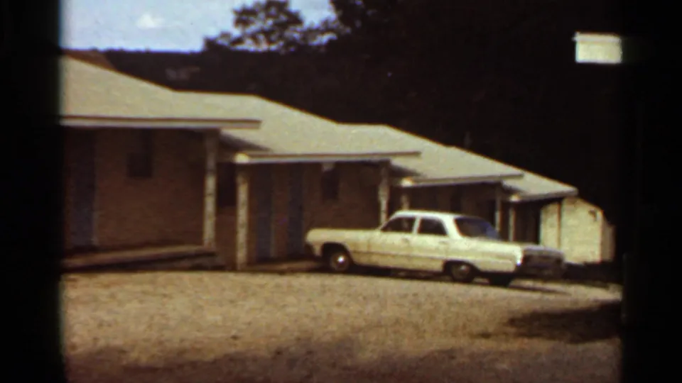 Kansas City motel exterior from 1965, showing a low building, covered walkway, gravel parking area, and white classic American car.