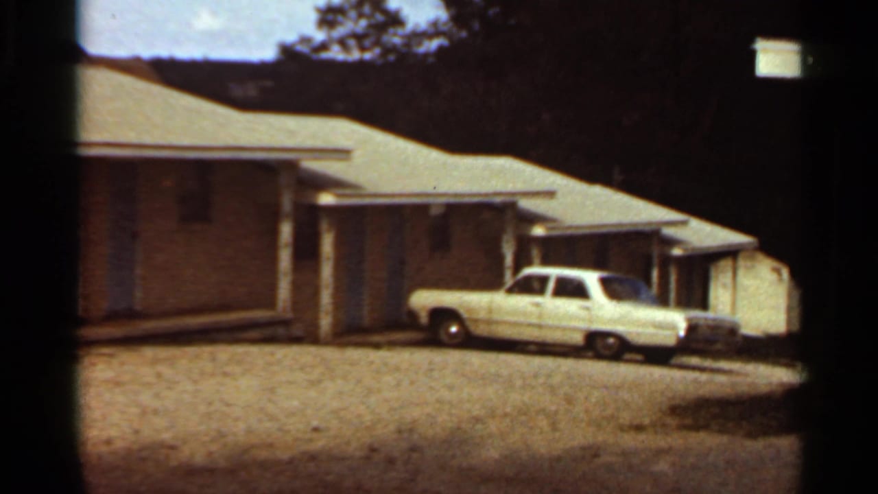 1965 8mm frame of a white American sedan outside a modest single-story residence in the Kansas City metadata context.