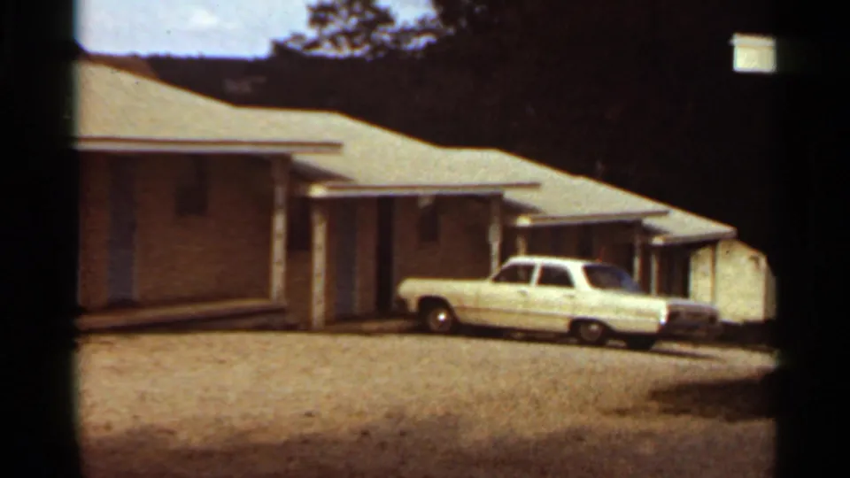 White sedan and modest house exterior remain in view, with trees behind and visible 8mm frame borders.