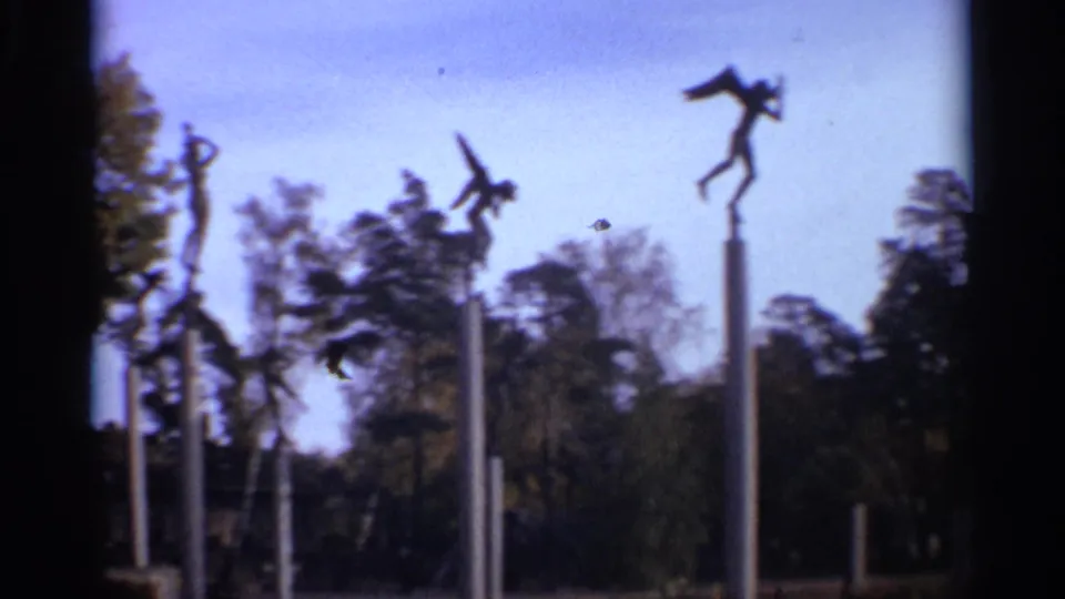 1965 Leningrad home-movie frame showing several stylized sculptures on poles above trees in a public park.