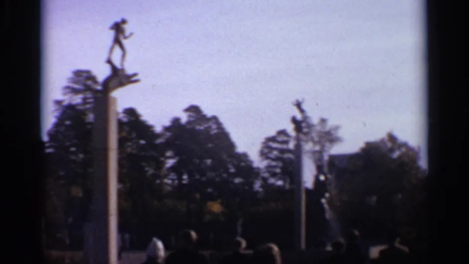 Home-movie view in Leningrad, 1965, showing a raised figure sculpture, trees, and distant park visitors.