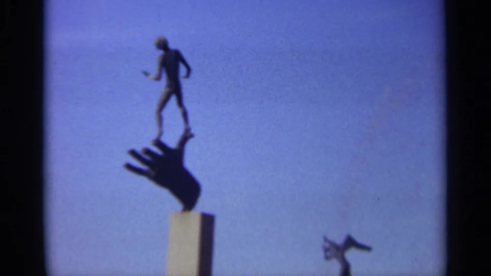 Modernist public sculpture in Leningrad, with a small human figure balanced above a large hand silhouette against open sky.