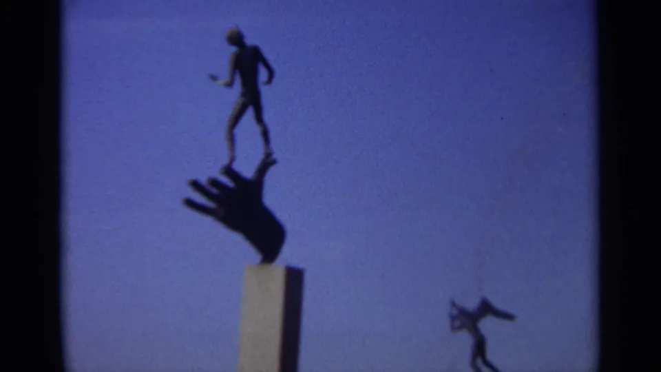 Closer 8mm view of the Leningrad sculpture, showing the figure and hand form in dark silhouette with sky filling the frame.