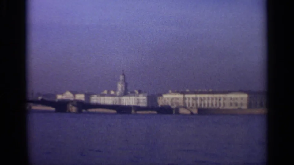 1965 Leningrad waterfront view with pale buildings, a distant spire, bridge spans, and wide water in soft 8mm color.