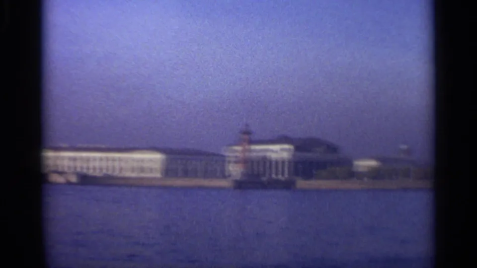 1965 8mm frame of Leningrad riverside architecture with a red marker tower and low skyline beyond the water.