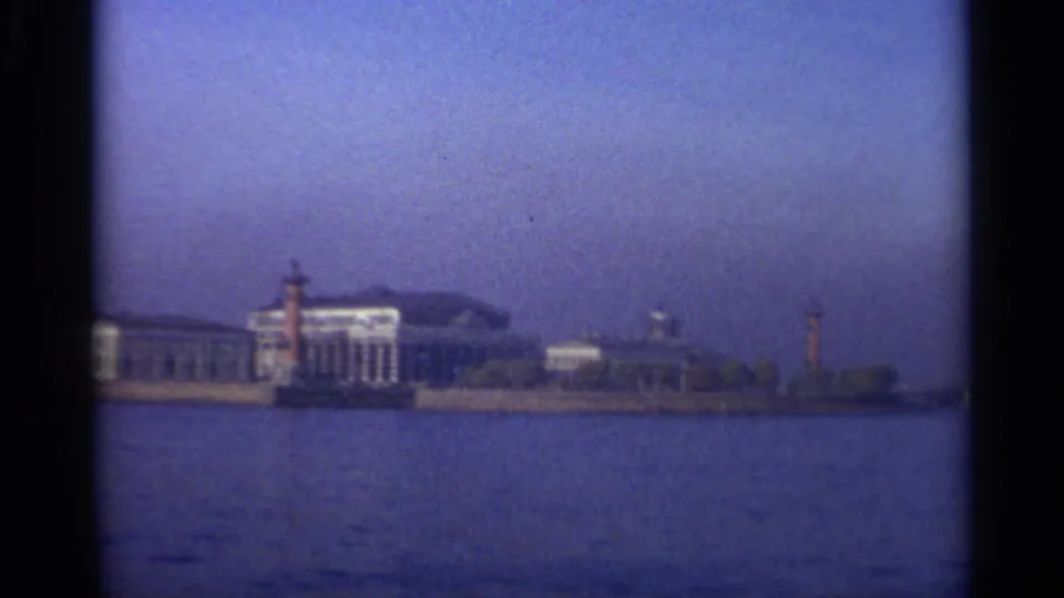End of the Leningrad waterfront pan with low riverside buildings, marker towers, open water, and blue-purple 8mm color cast.