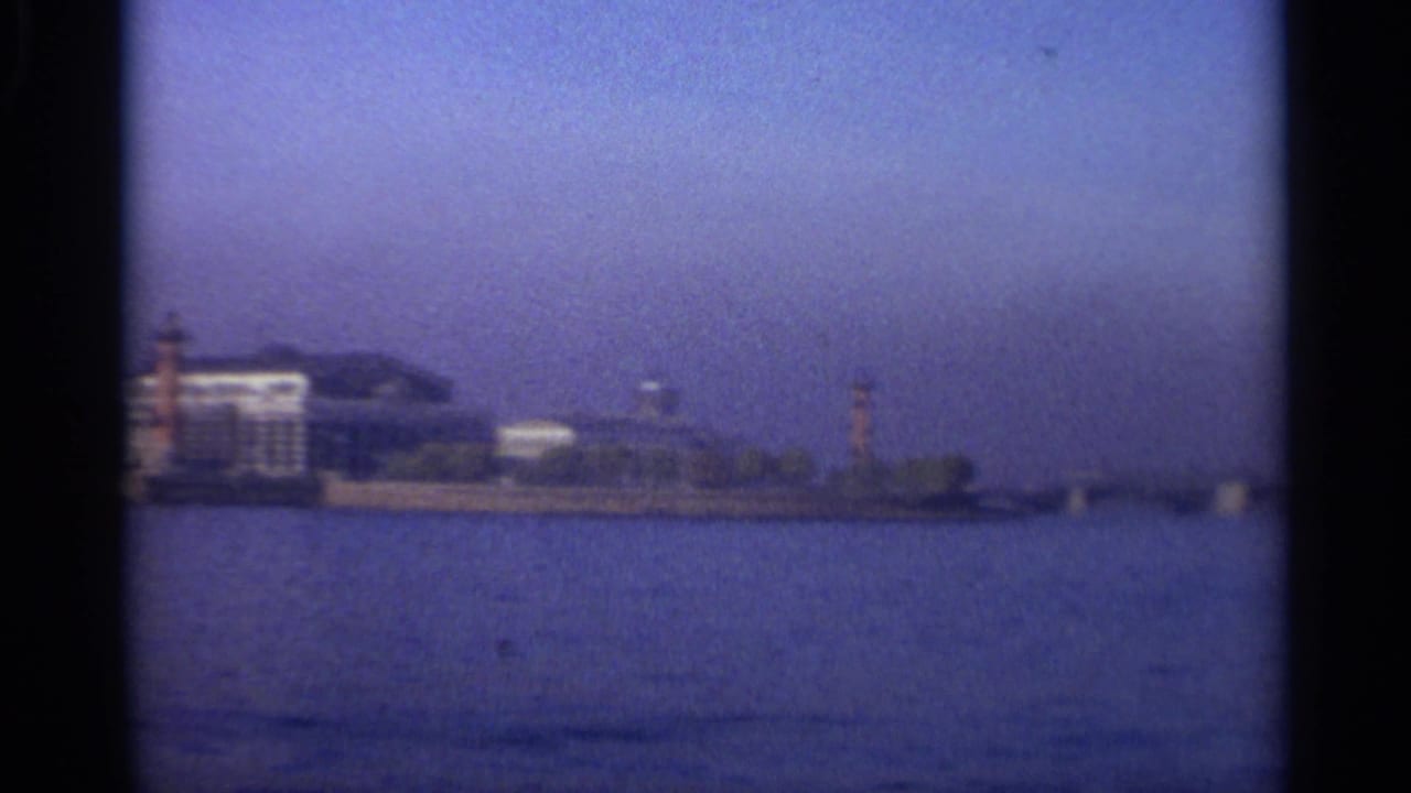 Distant waterfront buildings and a tower across blue water, framed by dark film edges.
