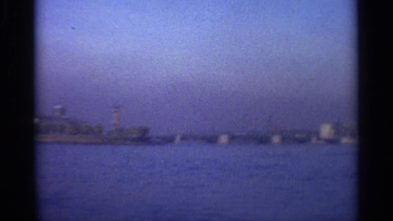 Waterfront panorama with a tower, low shoreline structures, and hazy blue sky.
