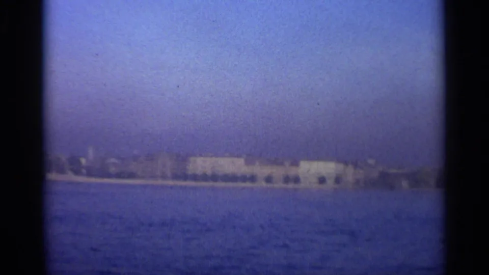 Final 1965 Leningrad waterfront view with a pale building complex, shoreline, and blue water under hazy sky.