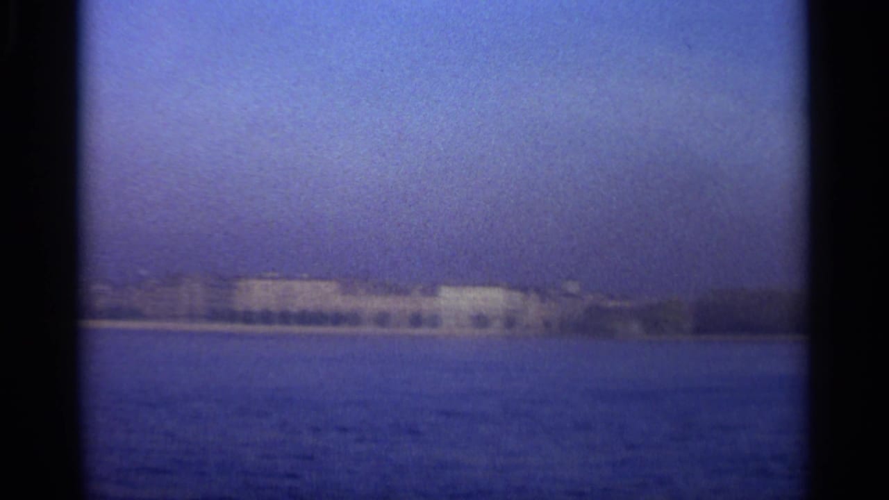 Distant waterfront buildings across blue water under a hazy sky.