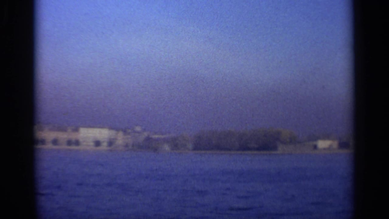 Shoreline with pale buildings and trees beyond open water.