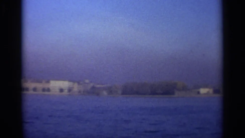 Leningrad shoreline with pale waterfront buildings and tree cover seen from the sea in 1965 footage.