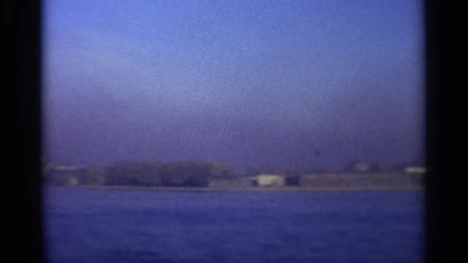 Soft 8mm frame showing a low Leningrad waterfront with small pale structures beyond blue water.