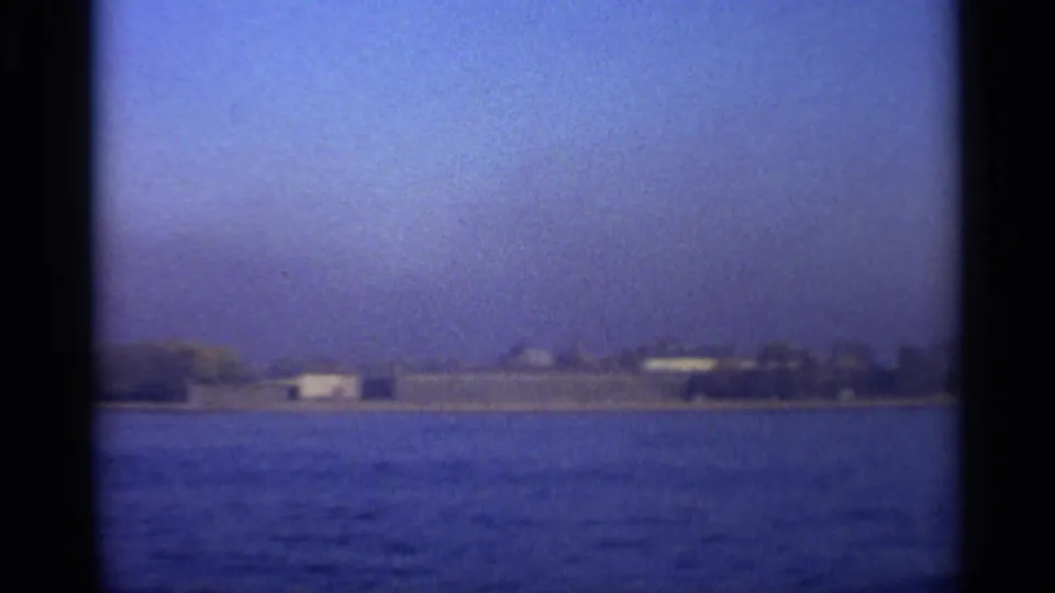 End of the 1965 waterfront pan, with a long low building and distant shore across rippled water.