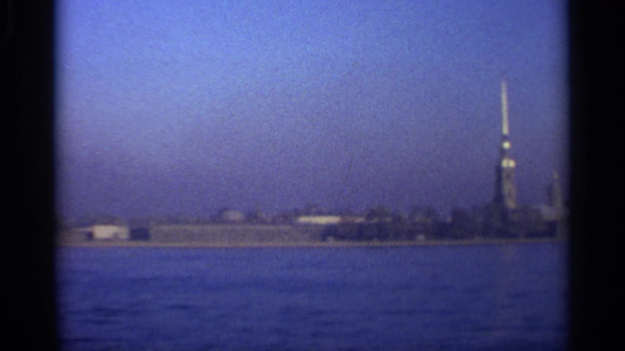 1965 Leningrad home-movie frame showing a distant fortress spire and low shoreline across blue water.