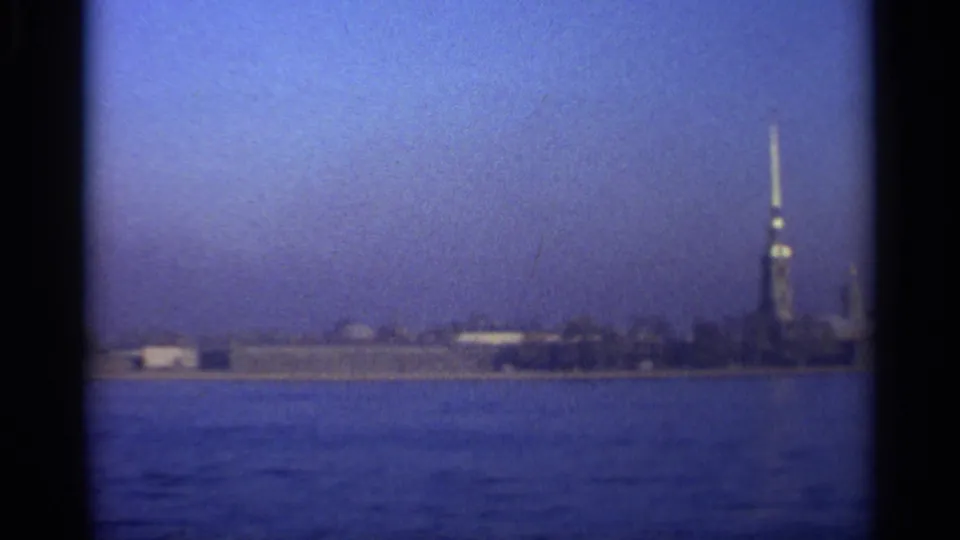 1965 Leningrad home-movie frame showing a distant fortress spire and low shoreline across blue water.