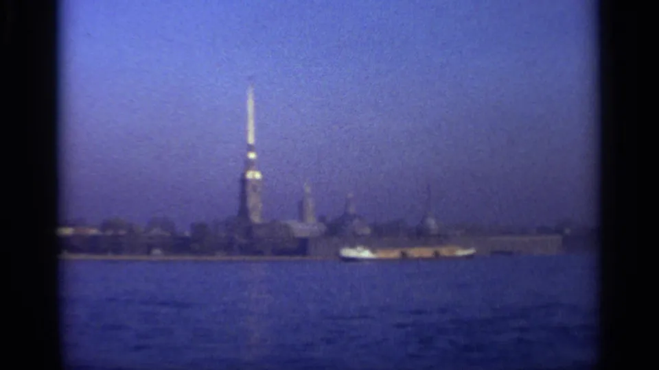 Soft 8mm frame of the Leningrad waterfront, with the fortress spire and a small boat passing across the foreground water.