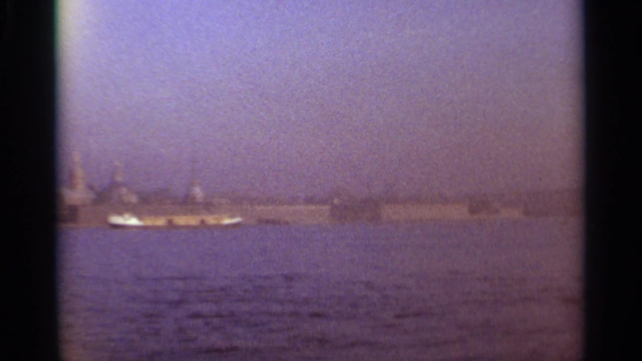 Distant waterfront city skyline across water with a small boat under a hazy sky.