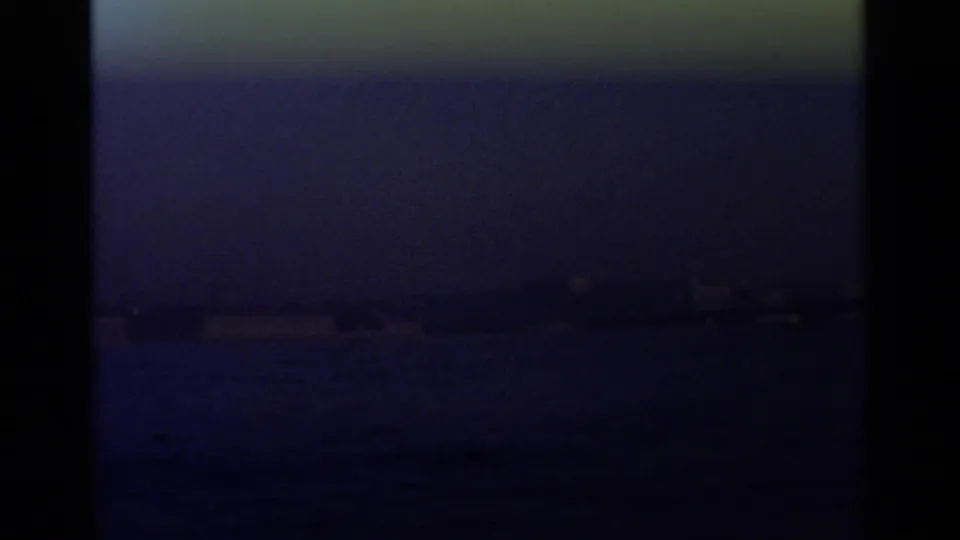 Dim 1965 8mm harbor view with water in the foreground and faint Leningrad waterfront forms in blue-purple exposure.
