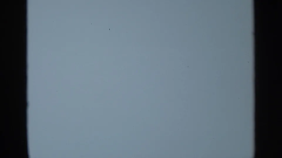 Pale blue blank or overexposed 8mm frame with dark film borders and minimal visible detail.