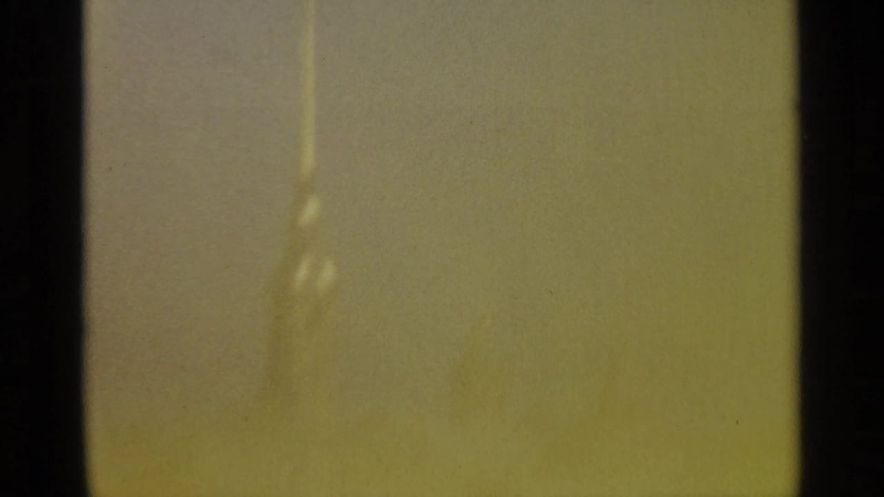 Yellow-green blank 8mm frame from the 1965 Leningrad clip, with gate-edge darkness and a faint vertical exposure mark.