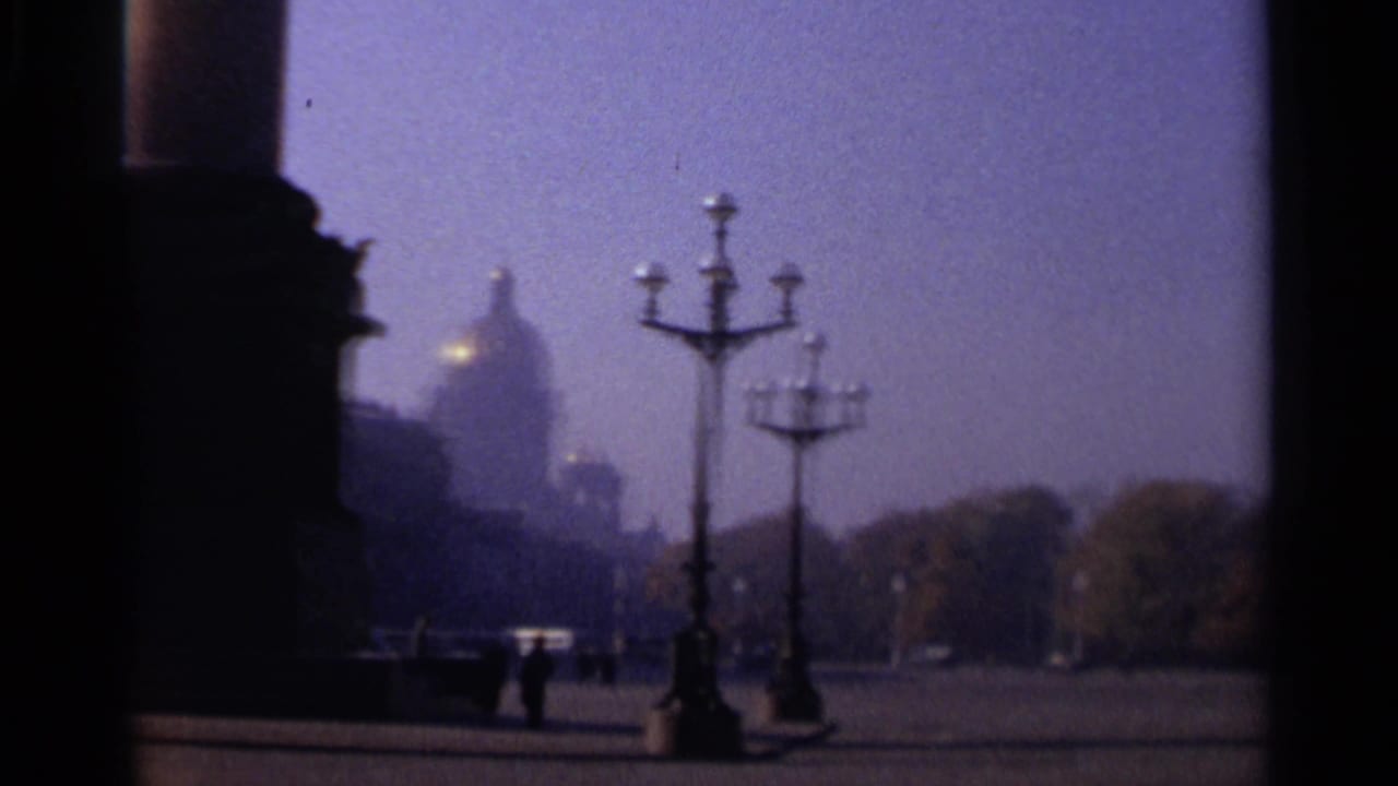 Hazy 1965 Leningrad square with ornate streetlamps, distant domed architecture, trees, open pavement, and small walking figures.