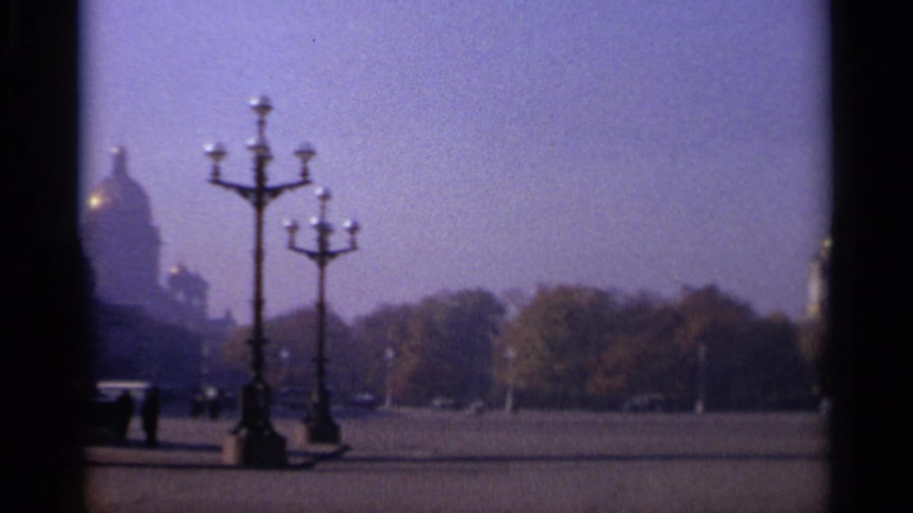 1965 Leningrad view across an open square, with silhouetted lamp posts, a distant domed cathedral, trees, and tiny pedestrians.