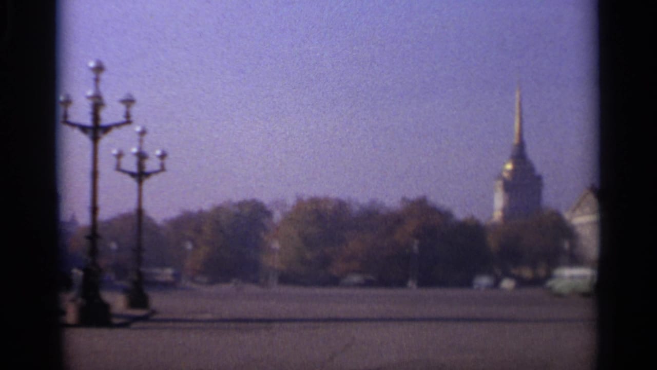1965 Leningrad home-movie view across a broad square with ornate lamps, trees, a distant gilded spire, and sparse vehicles.