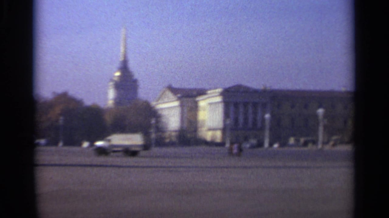 A panning 1965 Leningrad frame shows light traffic in front of classical architecture, trees, and a tall gilded spire.
