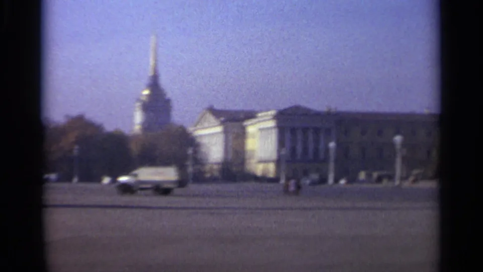 A panning 1965 Leningrad frame shows light traffic in front of classical architecture, trees, and a tall gilded spire.