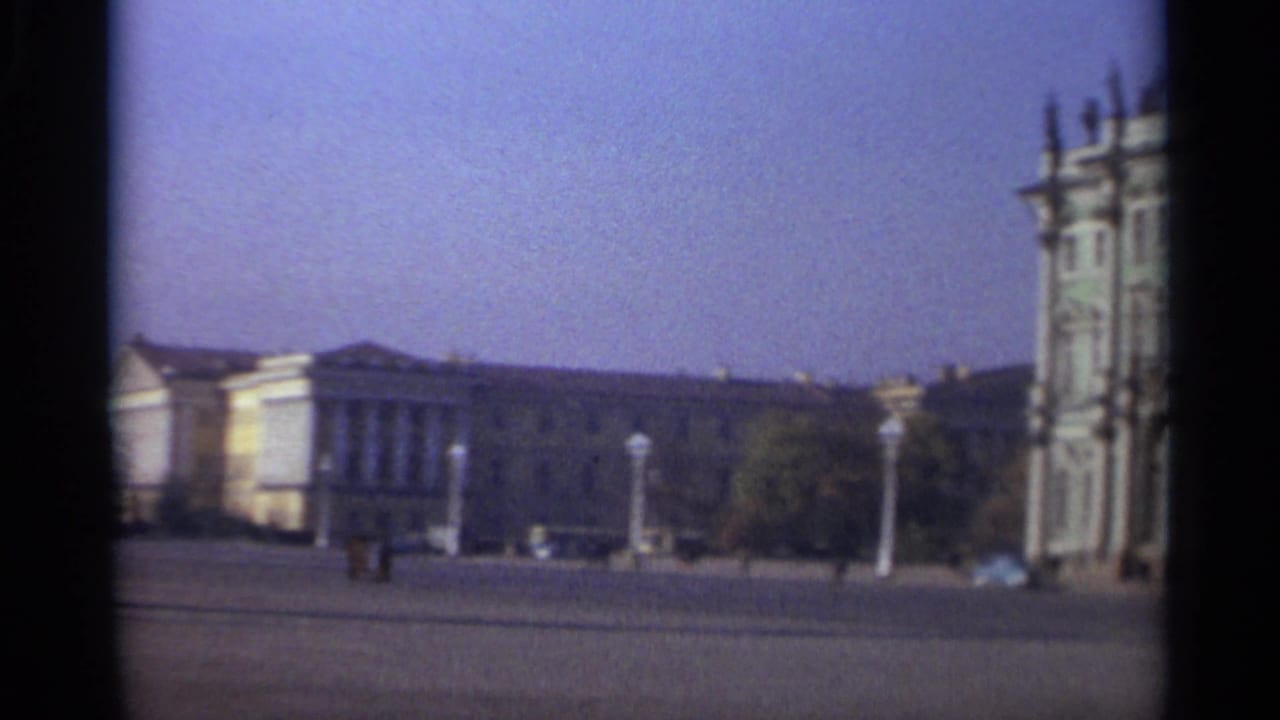 The pan settles on 1965 Leningrad architecture around a broad square, with tiny pedestrians, distant cars, and soft 8mm color shift.
