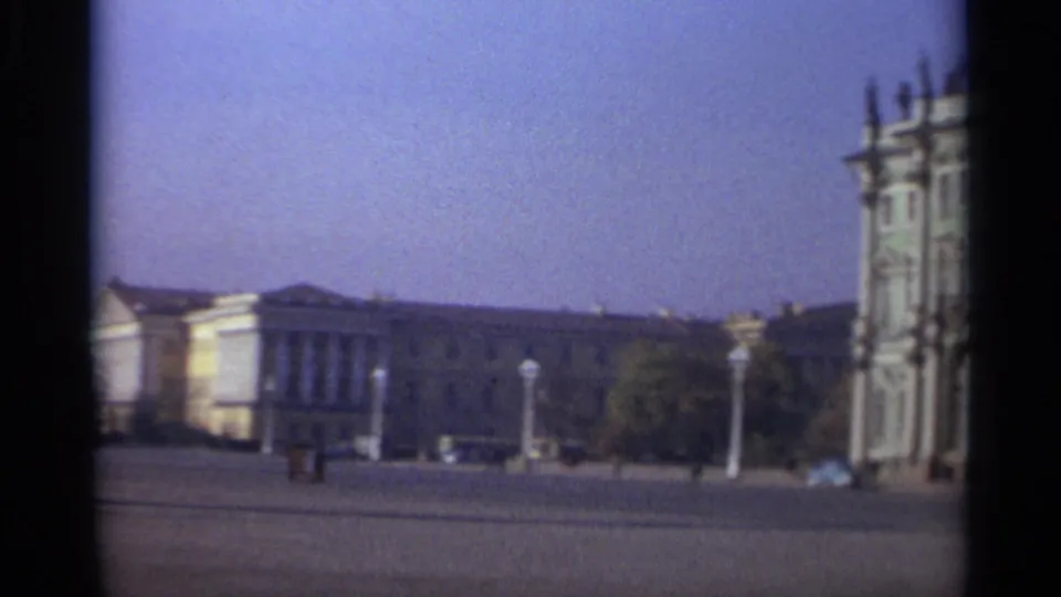 The pan settles on 1965 Leningrad architecture around a broad square, with tiny pedestrians, distant cars, and soft 8mm color shift.